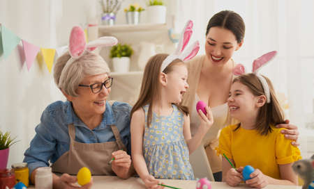 Mother, grandmother and daughters are painting eggs. Happy family are preparing for Easter. Cute...