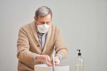 Old man wearing face mask and washing his hands during coronavirus and flu outbreak. Virus and illness protection, home quarantine. COVID-2019の写真素材
