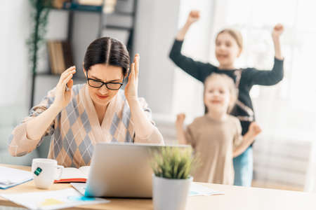 Woman working on a laptop. Noisy children and remote work from home.の写真素材