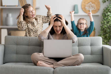 Woman working on a laptop. Noisy children and remote work from home.
