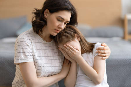 Mother is feeling sorry for a crying child. Mum is hugging her daughter.の写真素材