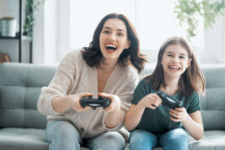 Happy family together. Mother and her child girl playing video games. People having fun at home.の写真素材