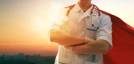 Doctor wearing facemask and superhero cape during coronavirus outbreak. Virus and illness...