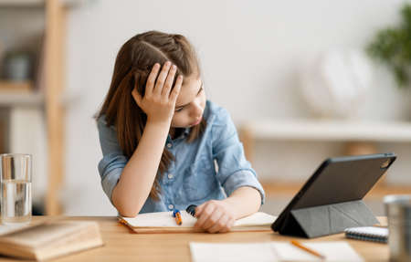 Back to school. Unhappy child is sitting at desk. Girl doing homework or online education.