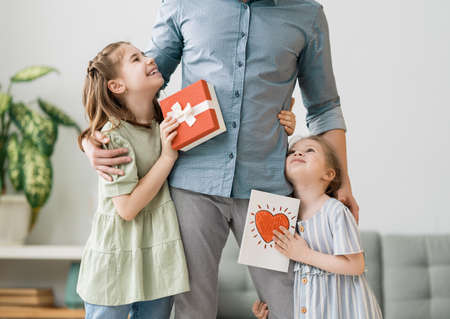 Happy father's day! Children daughters congratulating dad and giving him postcard. Daddy and girls...