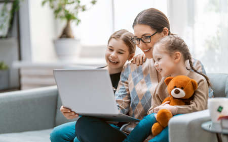 Happy loving family. Young mother and daughters girls using laptop. Funny mom and lovely children are having fun staying at home.の写真素材