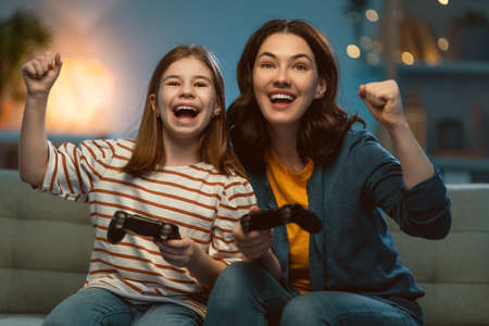 Happy family together. Mother and her child girl playing video games. People having fun at home.
