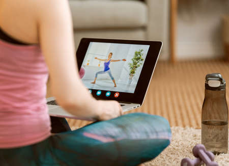 Young woman in activewear watching online courses on laptop while exercising at home.