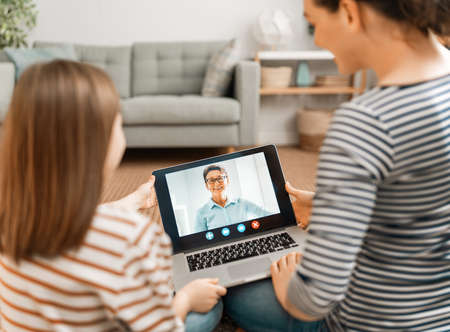 Happy loving family. Young mother and daughter girl using laptop pc for remote conversation with grandma. Funny mom and lovely child are having fun staying at home.の写真素材