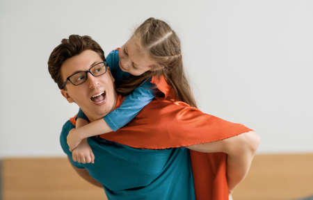 Father and his child playing together. Girl and dad in Superhero costume. Daddy and kid having fun, smiling and hugging. Family holiday and togetherness.の写真素材