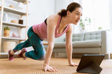 Young woman in activewear watching online courses on tablet while exercising at home.