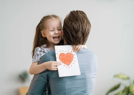Happy father's day! Child daughter congratulating dad and giving him postcard. Daddy and girl smiling and hugging. Family holiday and togetherness.の写真素材