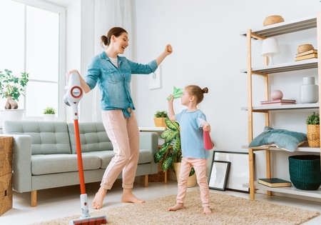 Happy family vacuuming the room. Mother and daughter doing the cleaning in the house.の写真素材