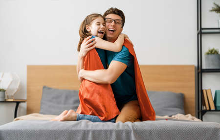 Father and his child playing together. Girl and dad in Superhero costume. Daddy and kid having fun, smiling and hugging. Family holiday and togetherness.の写真素材