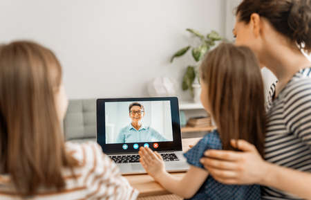 Happy loving family. Young mother and daughters girls using laptop pc for remote conversation with grandma. Funny mom and lovely children are having fun staying at home.の写真素材
