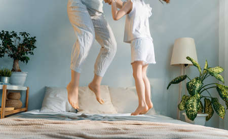 A nice child girl and her mother enjoy sunny morning and jumping on the bed. Good time at home.の写真素材