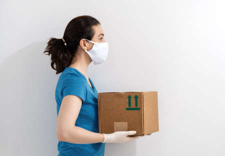 Delivery woman holding cardboard box in medical rubber gloves and mask. Online shopping. Quarantine.