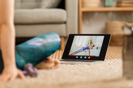 Young woman in activewear watching online courses on laptop while exercising at home.