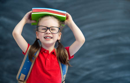 Back to school! Happy cute industrious child is learning in class on background of blackboard.