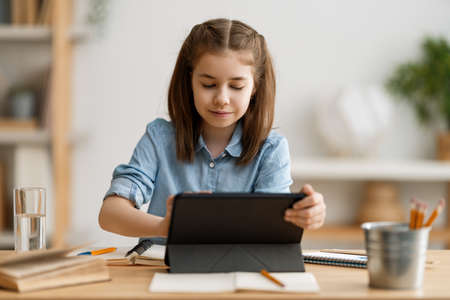 Back to school. Happy child is sitting at desk. Girl doing homework or online education.
