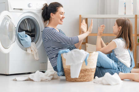 Beautiful young woman and child girl little helper are having fun and smiling while doing laundry at home.の写真素材