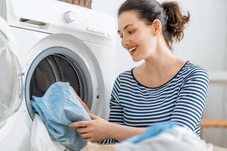 Beautiful young woman is smiling while doing laundry at home.の写真素材