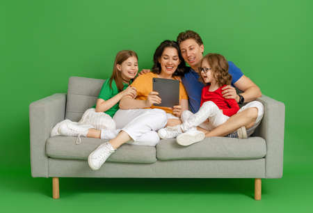 Happy loving family on bright color background. Father, mother and daughters girls using tablet pc...