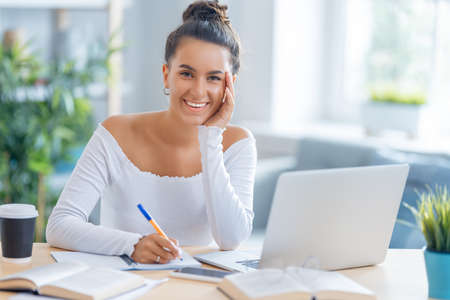 Focused young businesswoman studying online, watching webinar, podcast on laptop, making notes, sitting at work desk. E-learning concept.の写真素材