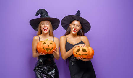 Happy Halloween! Two young women in black witch costumes with pumpkins on party on purple color background.の写真素材