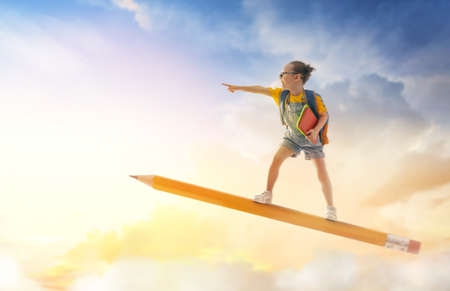 Back to school! Happy cute industrious child flying on the pencil on background of sunset sky. Concept of education and reading. The development of the imagination.の写真素材