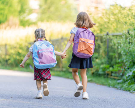 Pupils of primary school. Girls with backpacks outdoors. Beginning of lessons. First day of fall.の写真素材