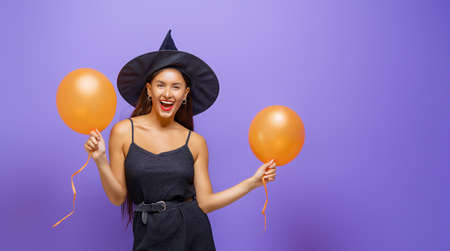 Happy Halloween! Young woman in black witch costume with air balloons on party on purple color...