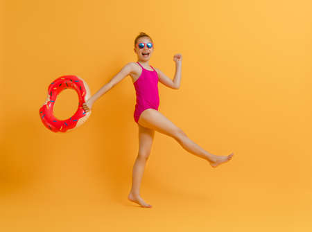 Happy child wearing swimsuit. Girl with swimming ring donut. Kid on a colored yellow background.の写真素材