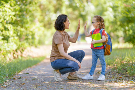 Parent and pupil of primary school go hand in hand. Woman and girl with backpack behind the back. Beginning of lessons. First day of fall.の写真素材