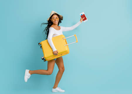 Go on an adventure! Happy woman going traveling. Young person with suitcase on color teal background.の写真素材