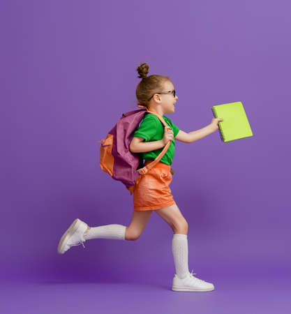 Back to school and happy time! Cute industrious child on color paper wall background. Kid with...