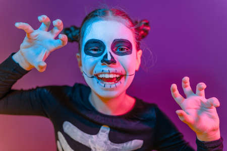 Happy Halloween! Cute little skeleton at party in colorful lighting.