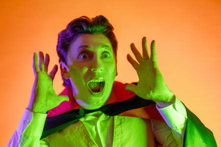 Happy Halloween! Young man in Dracula costume on party in color lighting.