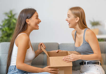 Beautiful young women are holding cardboard box sitting on sofa at home.の写真素材