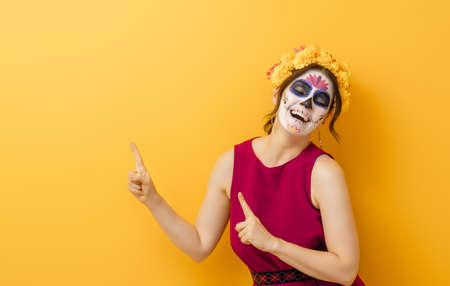 Adorable zombie in flower wreath posing on yellow background. Happy woman with Halloween creative...
