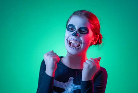 Happy Halloween! Cute little skeleton at party in colorful lighting.