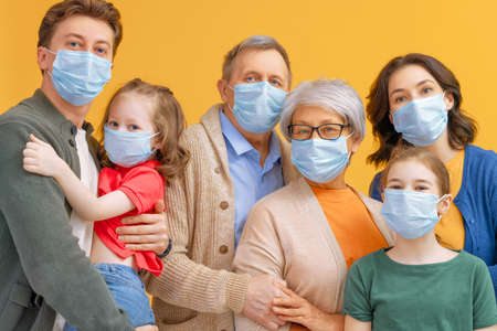 Family is wearing facemasks during coronavirus and flu outbreak. Virus and illness protection, quarantine. COVID-2019. Taking on masks. People on yellow wall background.の写真素材