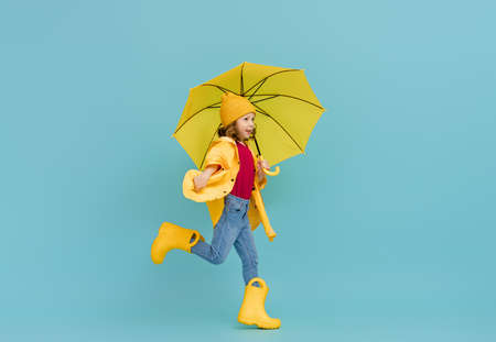 Happy emotional child laughing and jumping. Kid with yellow umbrella on colored teal background.の写真素材