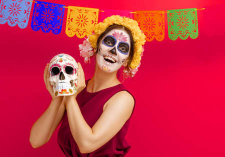 Adorable zombie in flower wreath posing on red background. Happy woman with Halloween creative...