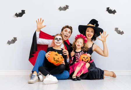 Mother, father and their kids having fun at party. Happy family celebrating Halloween. People wearing carnival costumes and makeup on white wall background.の写真素材