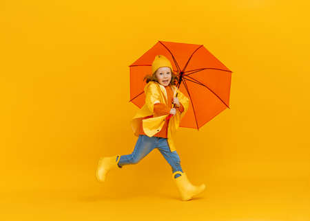 Happy emotional child laughing and jumping. Kid with orange umbrella on colored yellow background.の写真素材