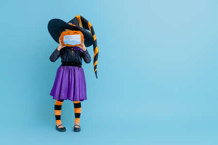 Happy Halloween! Cute little witch with a pumpkin  wearing face mask protecting from COVID-19.の写真素材
