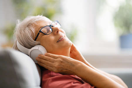 Senior woman listening to music in headphones sitting on the sofa in the room at home.の写真素材