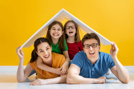 Mother, father and children girls with a symbol of roof on bright color background. Concept of housing for young family.の写真素材
