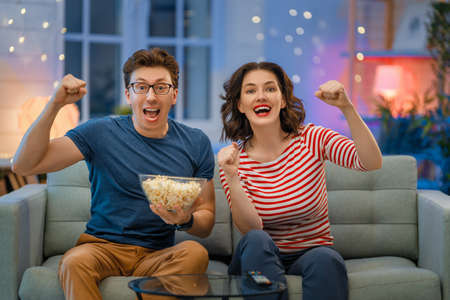 Happy family watching sport with popcorn in the evening at home. Couple spending time together.